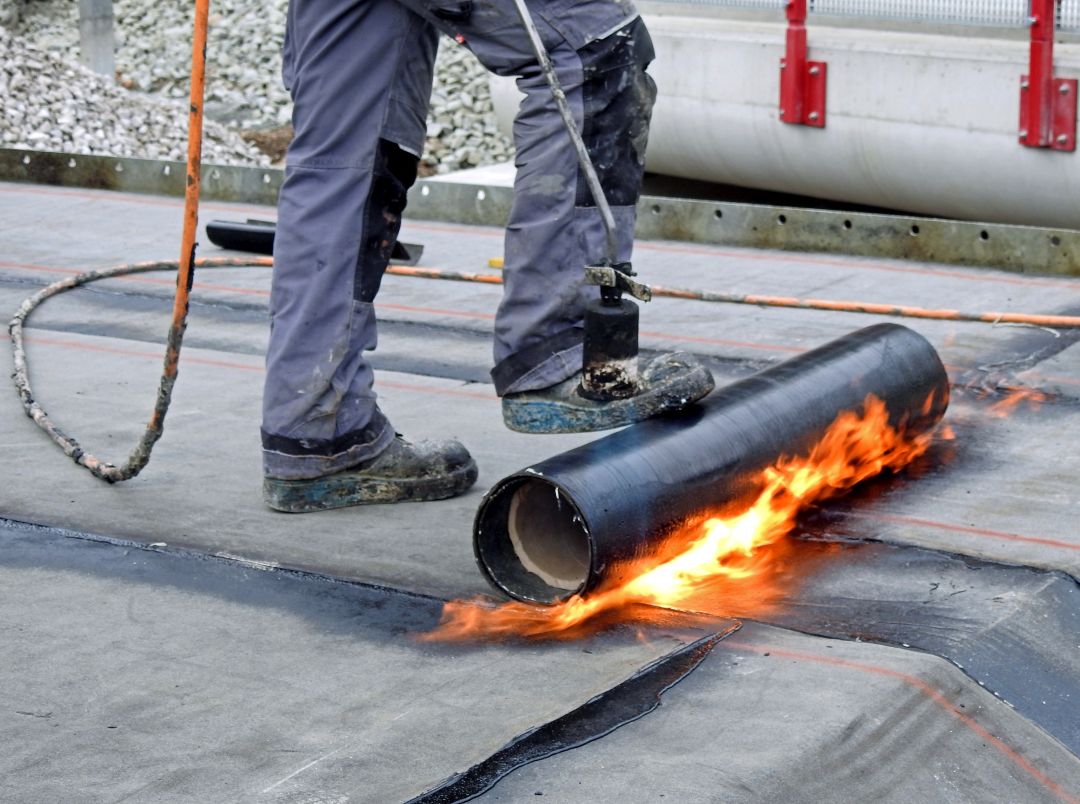 a commercial roofer completing a roof repair on a building using a torch