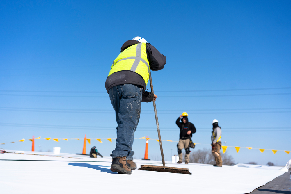 A construction worker installing a flat roof under a bright blue sky.