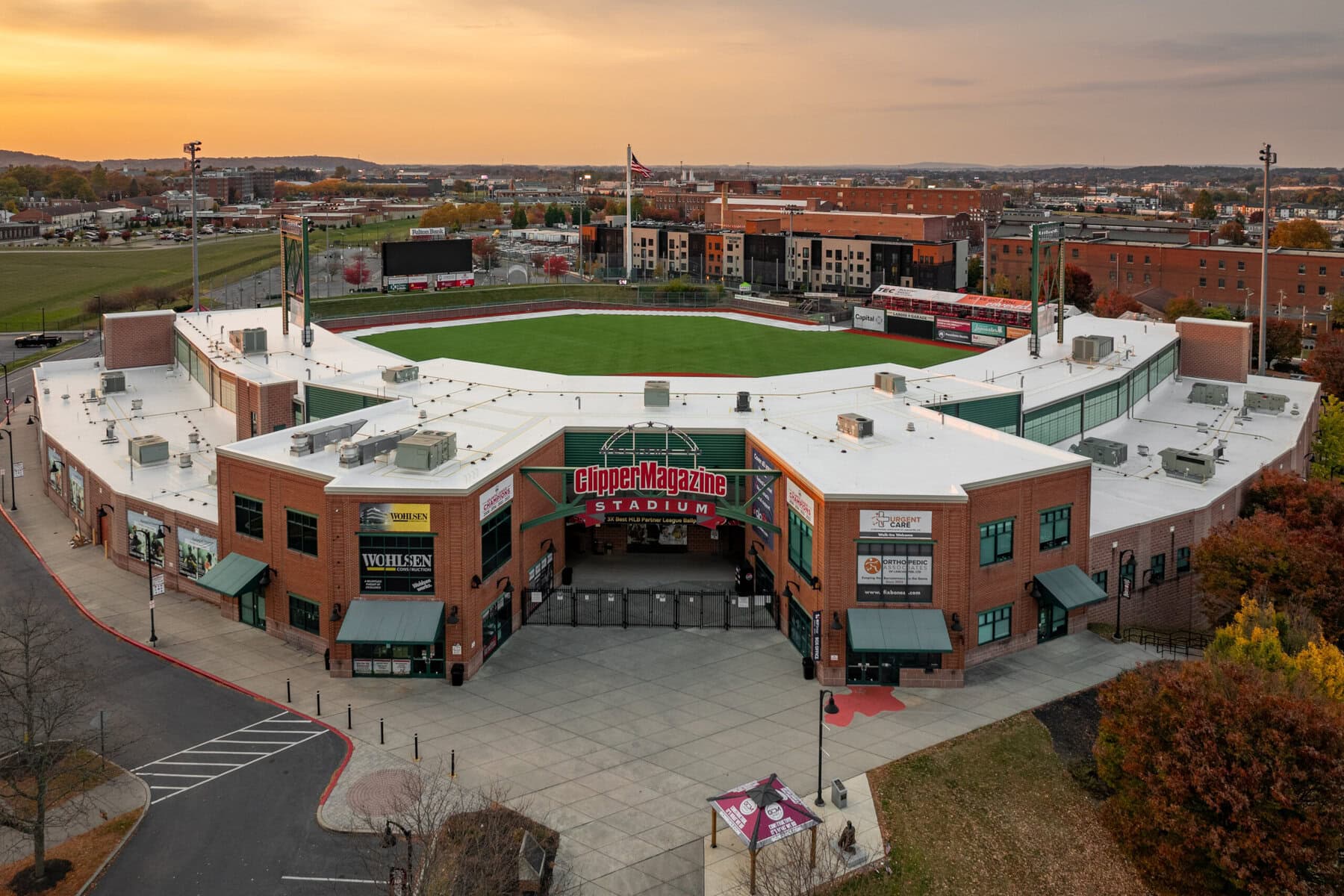 a baseball stadium with a green field and buildings in the background