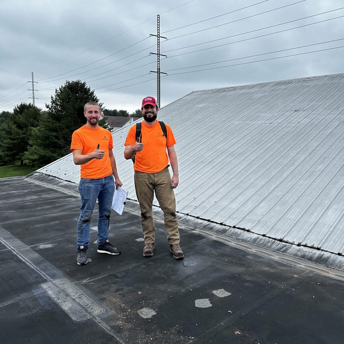 Two Moser team members standing on a roof with their thumbs up